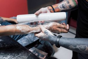 Frisch gestochenes Tattoo am Unterarm wird mit Folie abgedeckt – hygienische Nachsorge zur Vorbeugung von Hautreaktionen und Ausschlag.